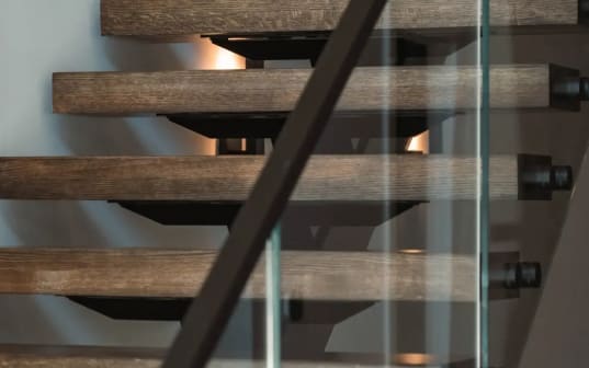 Stained oak floating treads with black standoff pins and a black handrail behind clear glass.