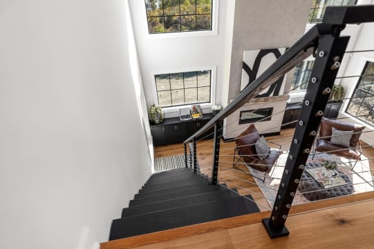 Black cable railing follows dark treads down into a bright living room with tall windows.