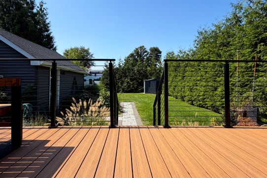 Black-post cable railing frames a new composite deck with a gate opening to a green backyard.
