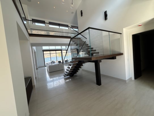 Dark floating treads on a black mono stringer with frameless glass railing rise to a glass-railed loft in a white double-height room.