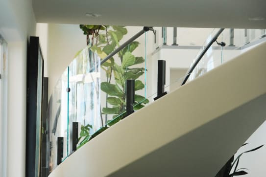 Curved glass panels on black talons with a black handrail sweep along a white curved stair stringer.