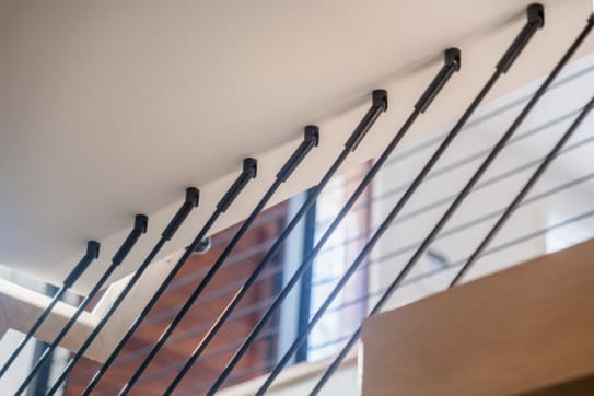 Close detail of black rods fastened directly into the ceiling above a stair.