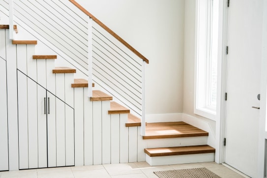 Slim white cable posts and an oak handrail follow a white stair with built-in storage by the front door.