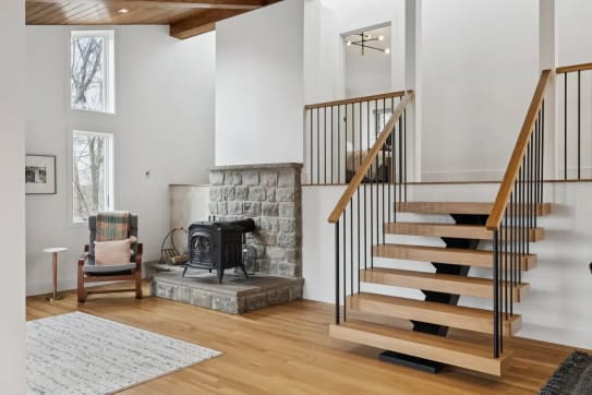 Oak-tread FLIGHT mono stair with black vertical balusters and wood handrail rises beside a stone wood-stove hearth.