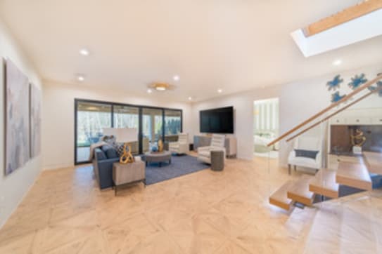 Floating wood treads with glass railing descend into a bright open living room with a skylight.