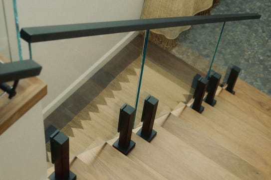 Black ascend talons hold frameless glass along oak treads beneath a black handrail.