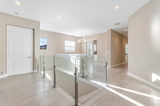 Stainless posts and handrail hold glass panels around a stair opening in a bright tiled hallway.