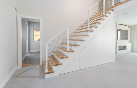 Natural oak replacement treads climb a white stair with white posts and horizontal cable railing in a bright home.