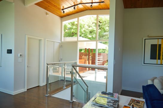 Stainless posts with glass panels and a round stainless handrail around a stair opening under a wood ceiling.
