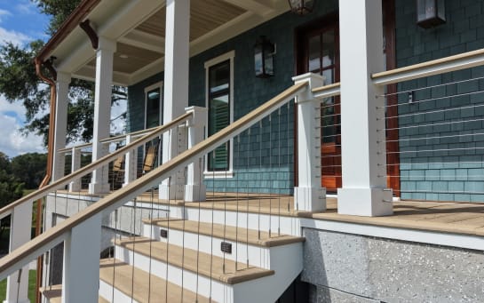 Close view of white posts and vertical cable railing along a porch stair on a blue-shingled home.