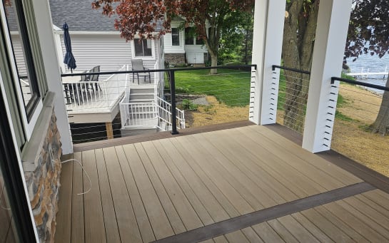 Black cable railing with white posts lines a covered composite porch overlooking a lake.