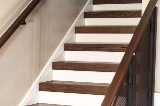 Rich brown thick-nose replacement treads over white risers alongside a wood-capped perforated panel railing.