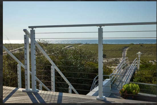 Silver posts with cable infill frame a dune path leading to the ocean from a coastal deck.