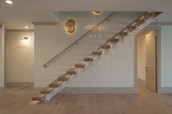 A floating oak-tread stair with under-tread LED lighting and a frameless glass guard against a white wall.
