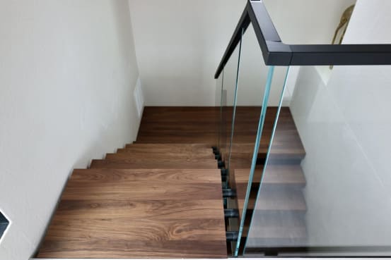 Looking down a walnut switchback stair with a frameless glass railing and black handrail.