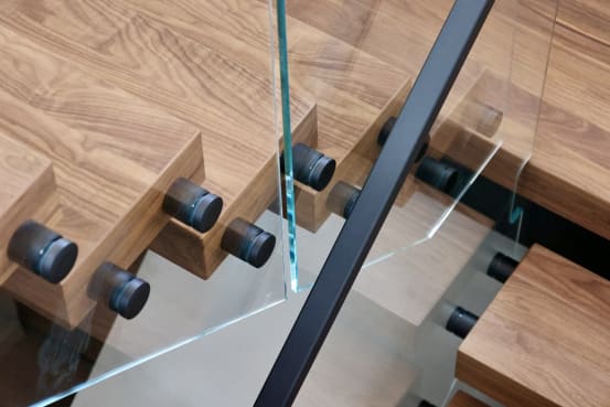 Close detail of black standoff pins securing frameless glass to the edges of thick walnut treads.
