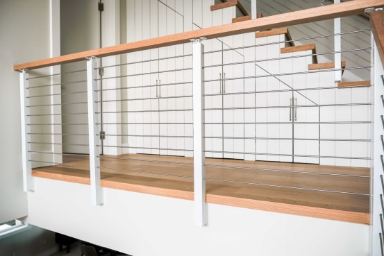 White slim side-mount cable posts with an oak handrail along a landing and a white paneled stair.