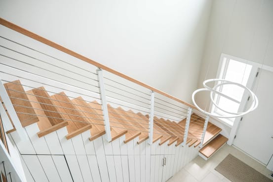 Oak treads and white side-mount cable railing descend a white paneled stair toward a bright entry.