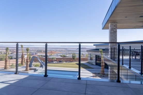 Black posts with Onyx rod infill and a hardwood cap rail line a terrace above a pool with desert views.