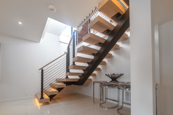A black center-stringer stair with thick oak treads and LED lighting, rod infill running up into the ceiling.