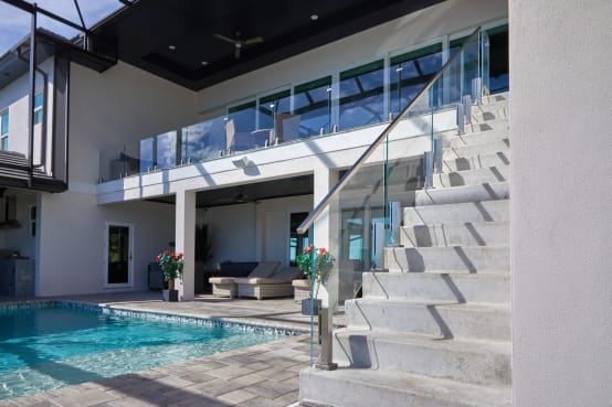 Concrete exterior stair beside a pool with frameless glass on talons and a stainless handrail, continuing along the upper balcony.