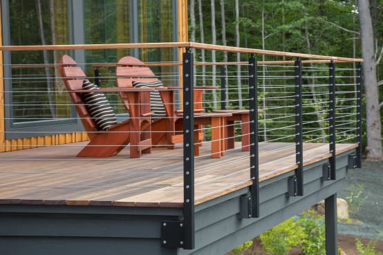 Hardwood deck with black side-mounted posts, stainless cables and a wood top rail beside red Adirondack chairs in the woods.