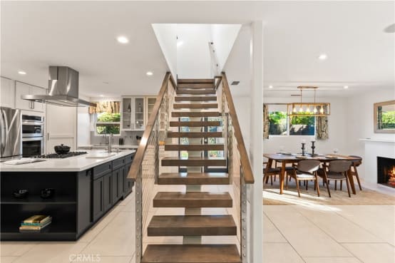 Wood floating treads on a mono stringer with cable railings rise between an open kitchen and dining room.