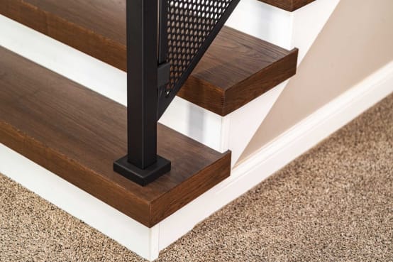 Close view of dark stained thick-nose replacement treads with a black post and perforated metal panel infill.
