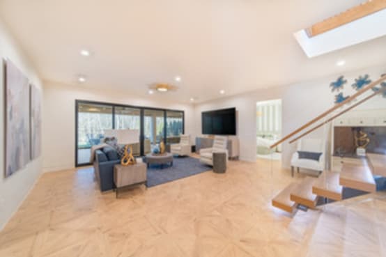 Floating wood treads with glass railing descend into a bright open living room with a skylight.