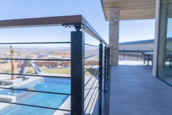 Black posts with Onyx rods and a thermally treated hardwood cap rail along a terrace above a pool.