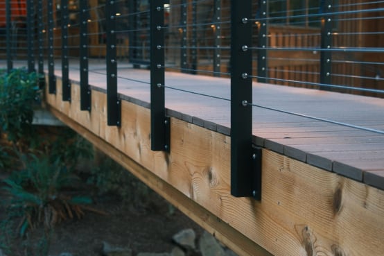 Black side-mount posts with cable infill fixed to the timber fascia of an elevated walkway.