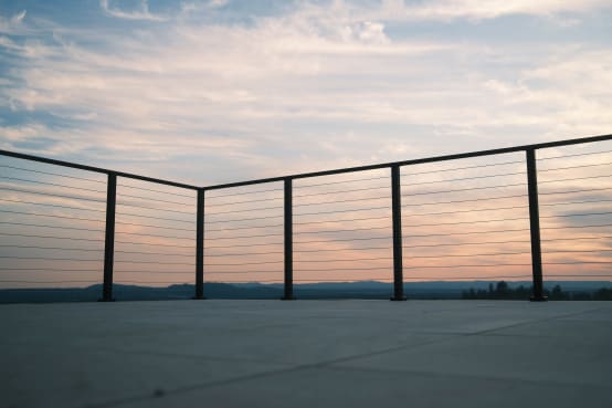 Black-post cable railing frames a rooftop terrace against a sunset sky and distant hills.