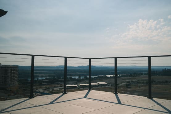 Black cable railing wraps a paved rooftop terrace overlooking a river valley.