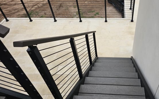 Black cable railing follows exterior stairs down along a smooth stucco wall