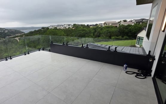 Frameless glass on talon spigots edges a large tiled terrace overlooking hills and a lake