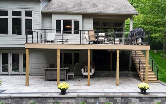 Elevated composite deck and stair with black cable railing above a stone patio.
