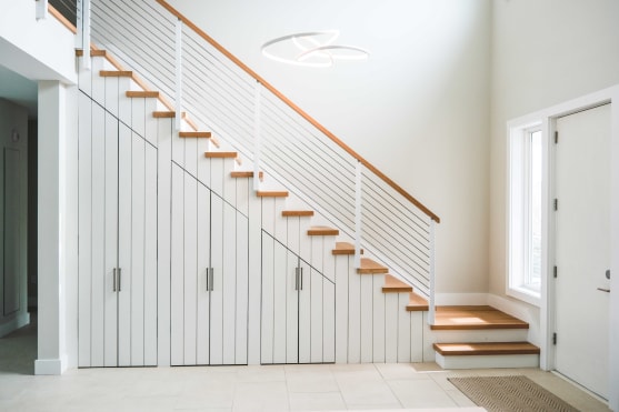 Oak treads and white cable railing with a wood cap climb over built-in under-stair cabinets in a bright entry.