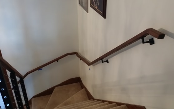 Dark wood handrail on black wall-mount brackets follows a carpeted switchback stair.