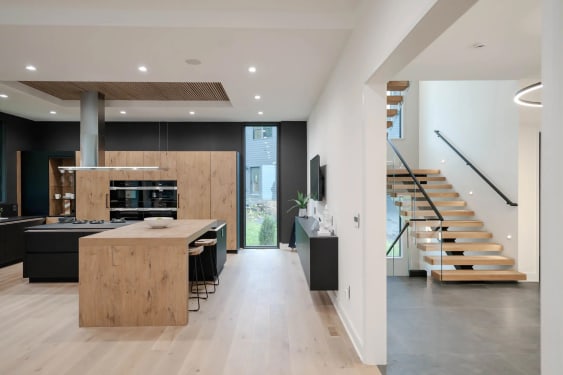 Open modern kitchen leading to an oak floating stair with glass railing and black wall handrail.