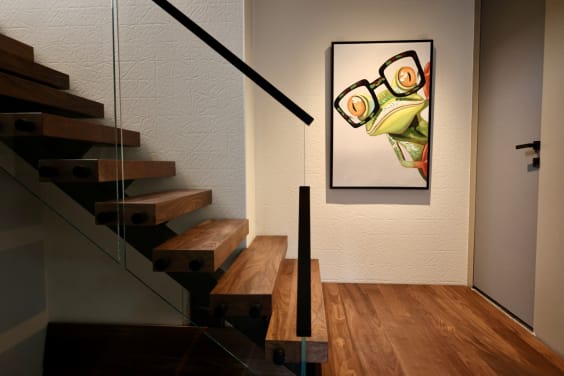 Walnut floating treads on a black stringer with frameless glass mounted by black standoffs and a slim black handrail beside framed art.