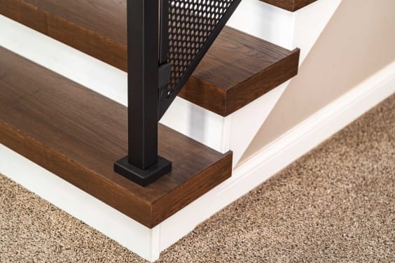 Close view of dark stained thick-nose replacement treads with a black post and perforated metal panel infill.