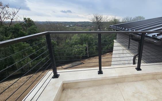 Black cable railing atop a limestone kneewall on a roof terrace overlooking treetops