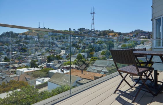 Frameless glass railing wraps a composite deck with bistro chairs overlooking hillside city homes and a radio tower.