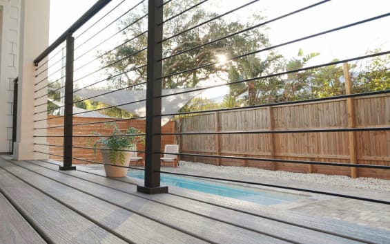 Low-angle view of black posts and horizontal rods along a gray deck overlooking a pool.