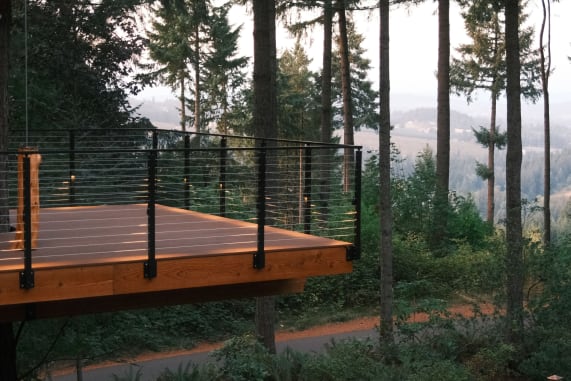 A cedar platform with black side-mount cable railing overlooks a misty forested valley.