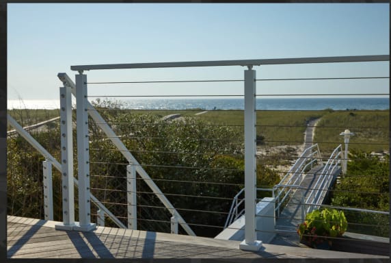 Silver posts with cable infill frame a dune path leading to the ocean from a coastal deck.