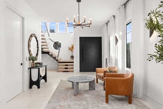 Styled white foyer with a floating stair and glass guard rising to a landing behind the seating area.