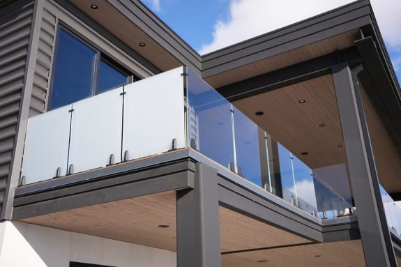 A modern balcony with frosted and clear glass panels on talon clamps beneath a wood soffit.
