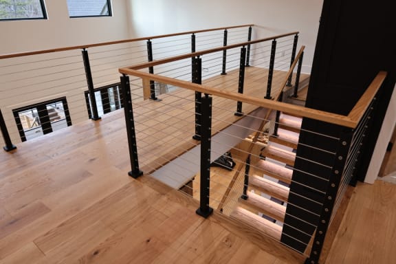 Black-post cable railing with ash handrails wraps a stair opening with LED-lit treads below