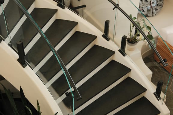Curved frameless glass on black talons with a curved handrail follows a white curved stair with black treads.